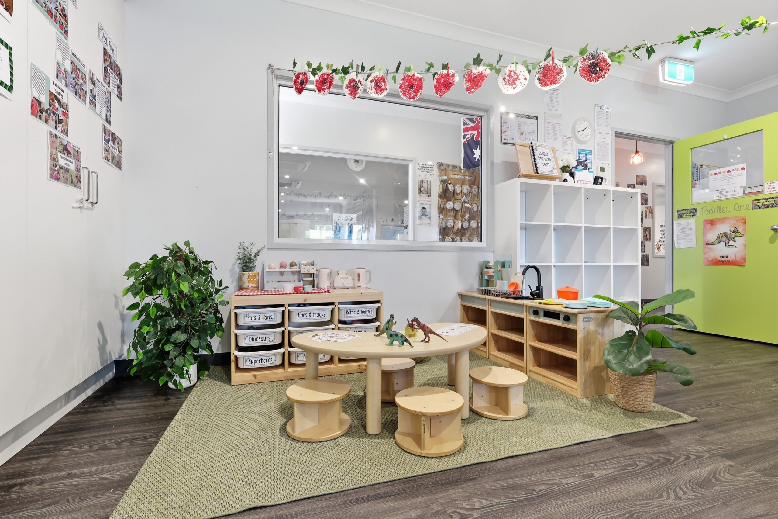 Toddler room at Walkerston Early Learning with a low round table, timber stools, labelled toy storage and a play kitchen